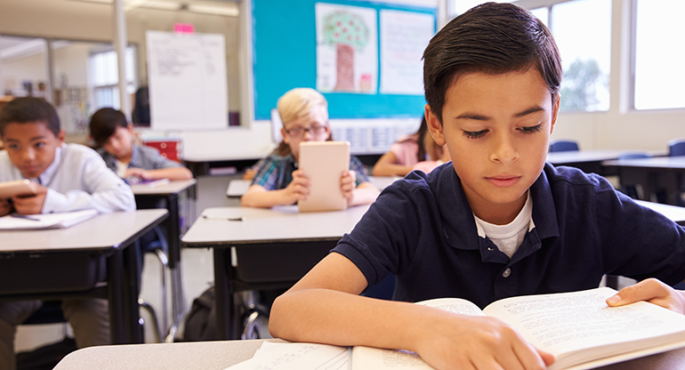 En pojke läser i en bok i ett klassrum. Foto.