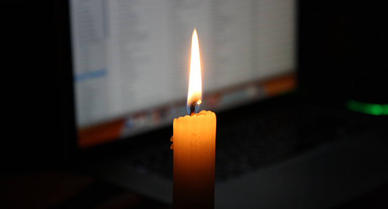 Ett tänt stearinljus framför en bärbar dator. Foto.