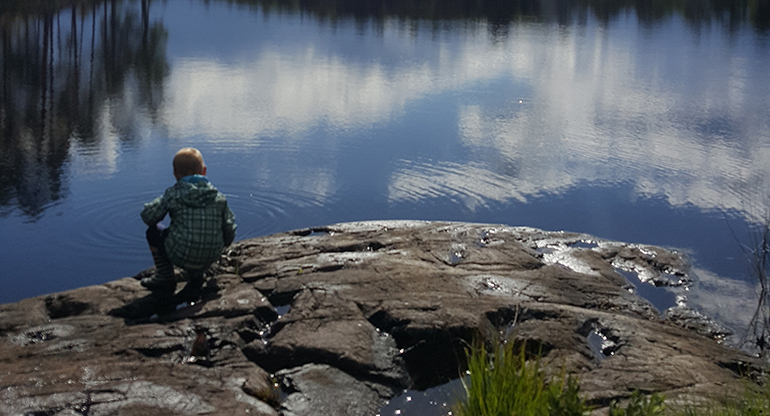 En pojke på en klippa vid en sjö. Foto.