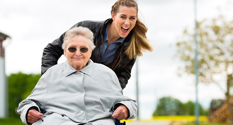 En ung kvinna kör en äldre kvinna i en rullstol. Foto.