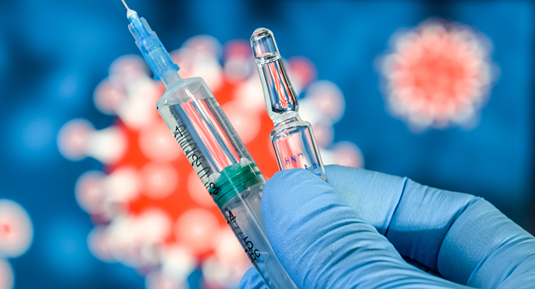 En hand i blå handske håller i en vaccinspruta. Foto.