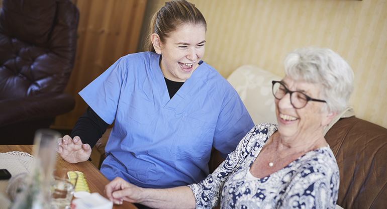En personal från hemtjänsten skrattar tillsammans med en äldre kvinna. Foto.