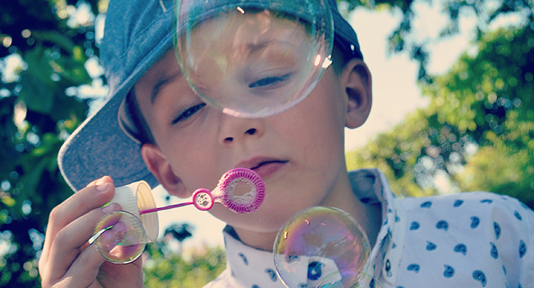 En pojke blåser såpbubblor. Foto.