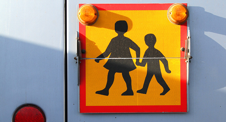 En skolbusskylt med två tecknade barn.