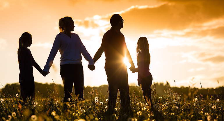 En familj som håller varandra i händerna i solnedgången. Foto.