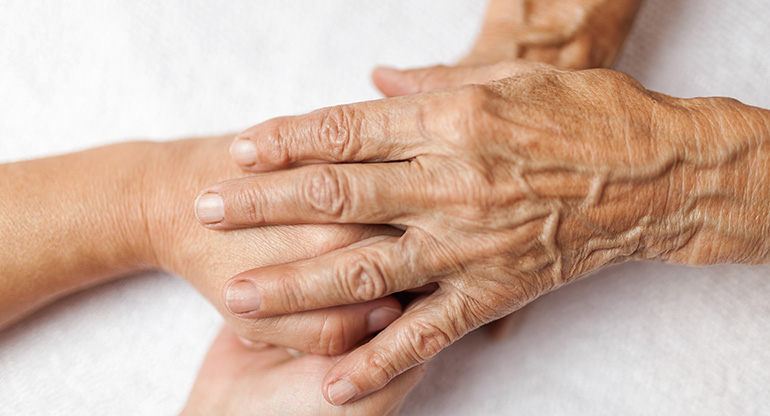 En gammal person håller sina händer på en ung persons händer. Foto.