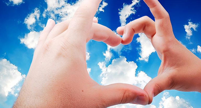Två händer formar ett hjärta mot himlen. Foto.